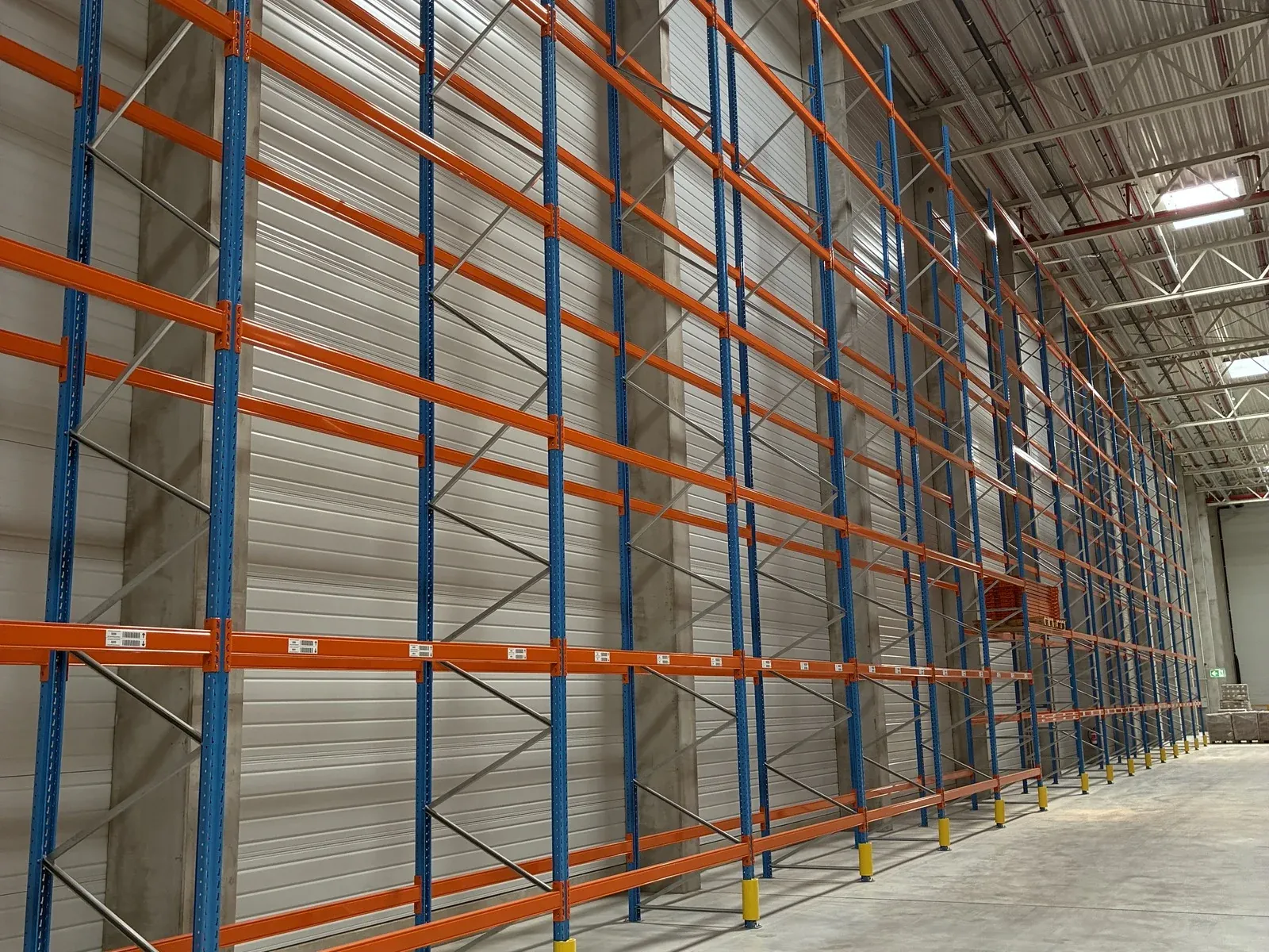 Hohe Palettenregalanlage in blau-orange entlang einer Hallenwand, vor der Demontage.